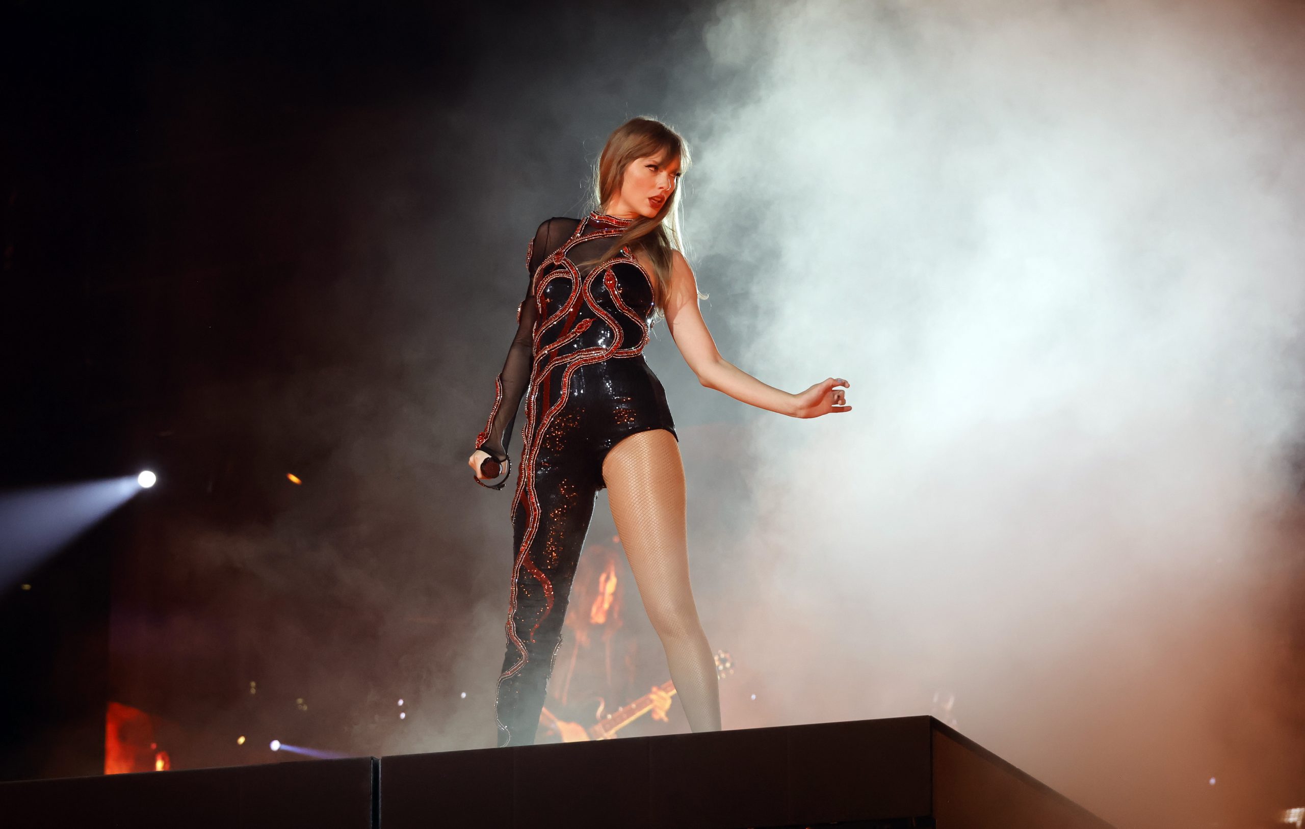 Taylor Swift on stage with a black unitard and red applique with fog behind her...